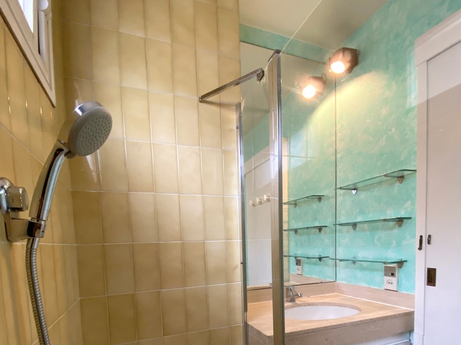 La salle de bains avec baignoire et son pare-douche, et un meuble-lavabo avec dessus en marbre.