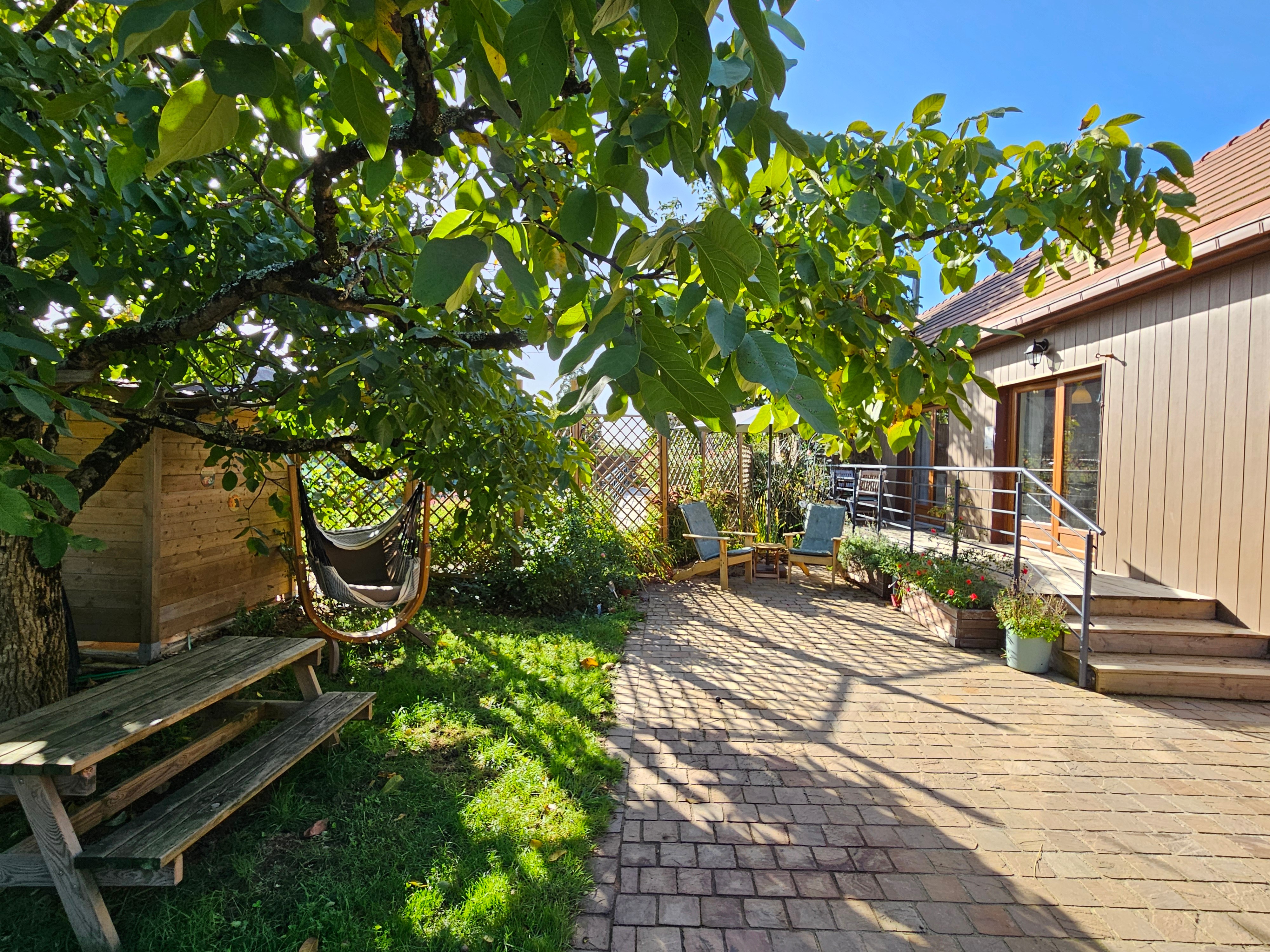 Agréables extérieurs avec une terrasse attenante à la pièce de vie, et une cour avec transats et jardinet ombragé sous le noyer.