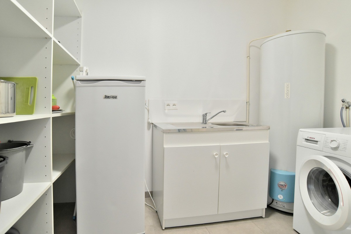 Arrière-cuisine avec second réfrigérateur et évier. Espace buanderie à droite avec lave-linge.