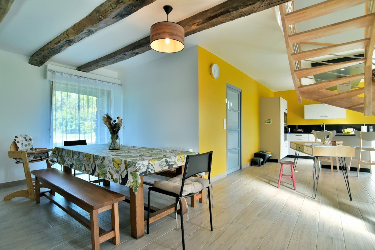 Grande pièce de vie avec poutres apparentes. En enfilade coin salon, coin séjour, coin bureau et coin cuisine.