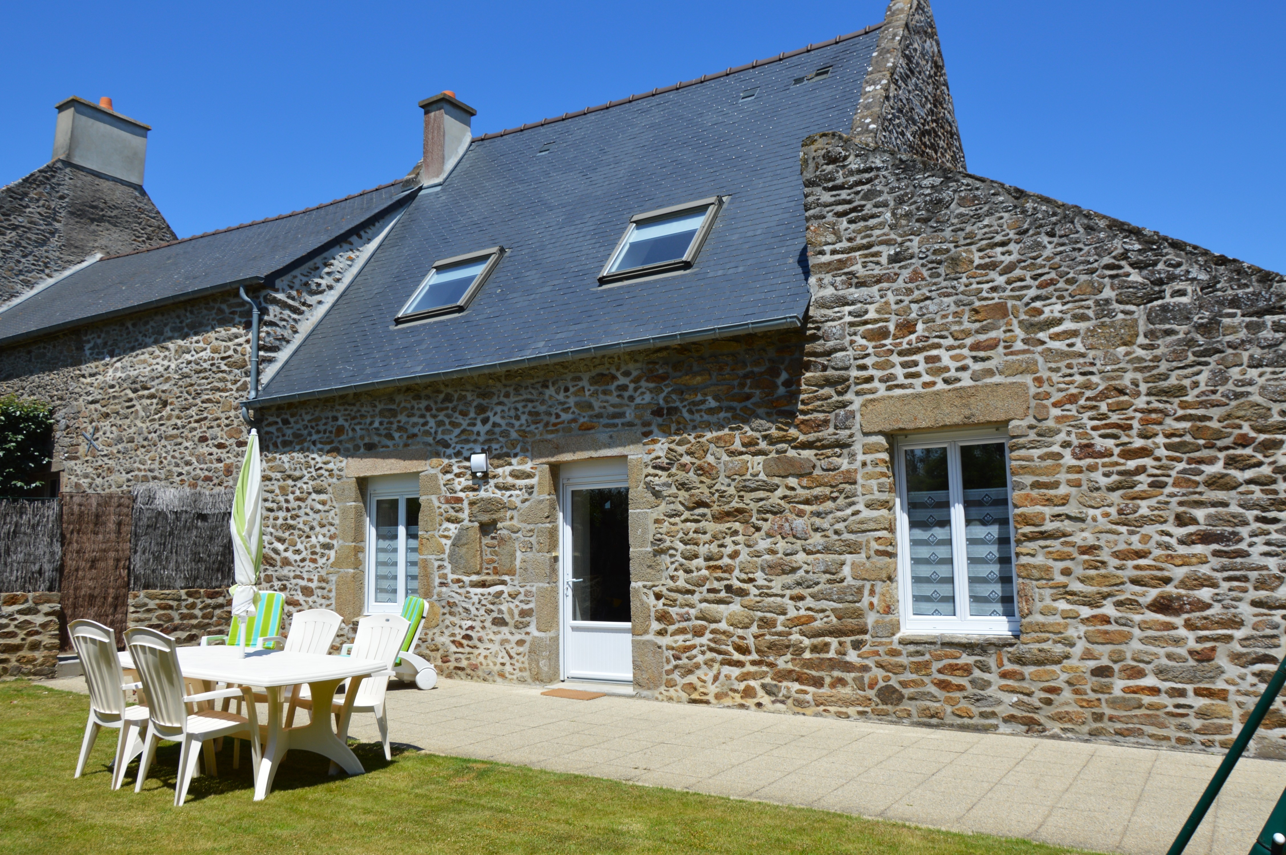 Façade en pierre du Gîte 2 avec terrasse, jardin, balançoire, bac à sable et stationnements privatifs. Accès indépendant.