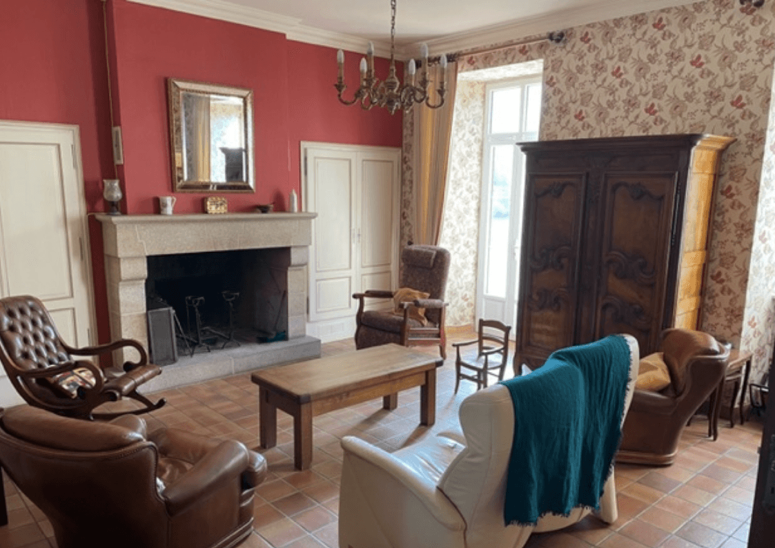 Salon lumineux avec cheminée en pierre, fauteuils en cuir et décoration chaleureuse dans une maison de caractère à Saint-Simon