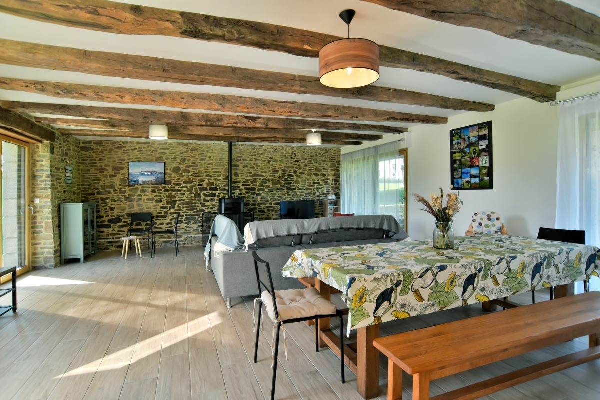 Grande pièce de vie avec poutres apparentes. En enfilade : coin salon, coin séjour, coin bureau et coin cuisine.