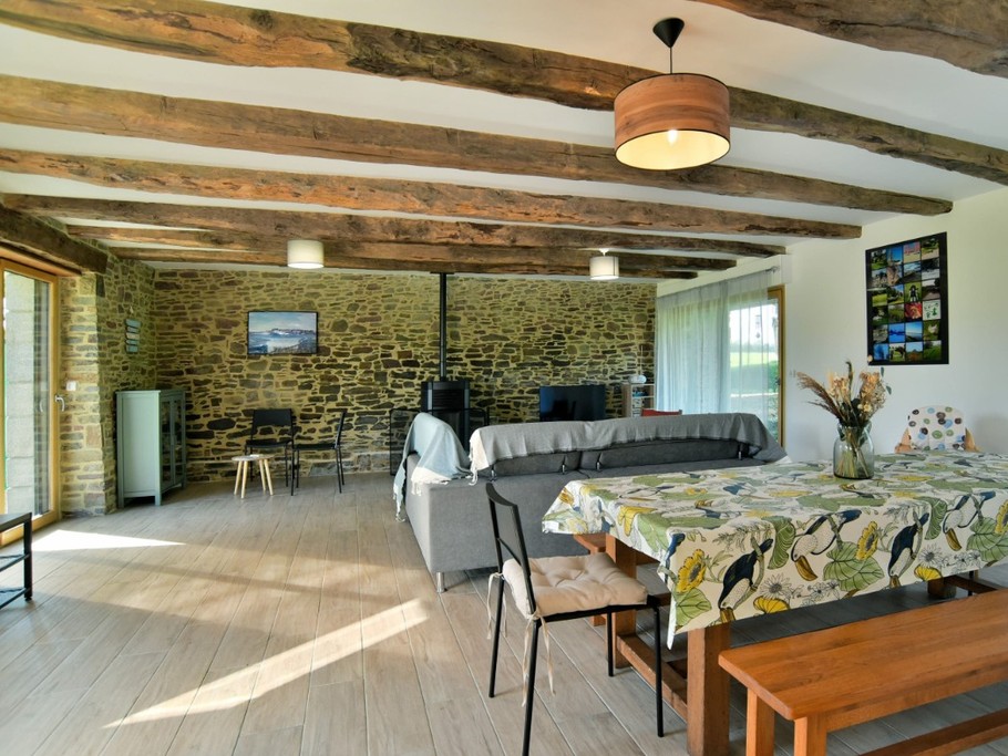 Grande pièce de vie avec poutres apparentes. En enfilade : coin salon, coin séjour, coin bureau et coin cuisine.