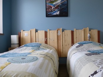 Chambre bleue avec deux lits simples, placard et TV.