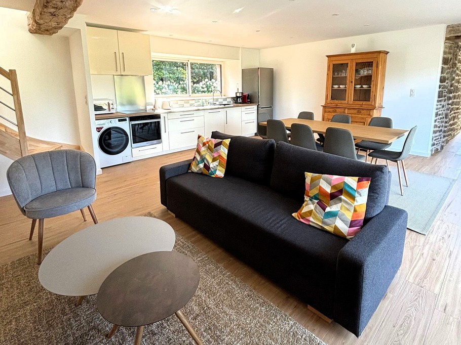 Grande pièce de vie avec salon (poêle à bois, smart TV), séjour et cuisine ouverte parfaitement équipée.