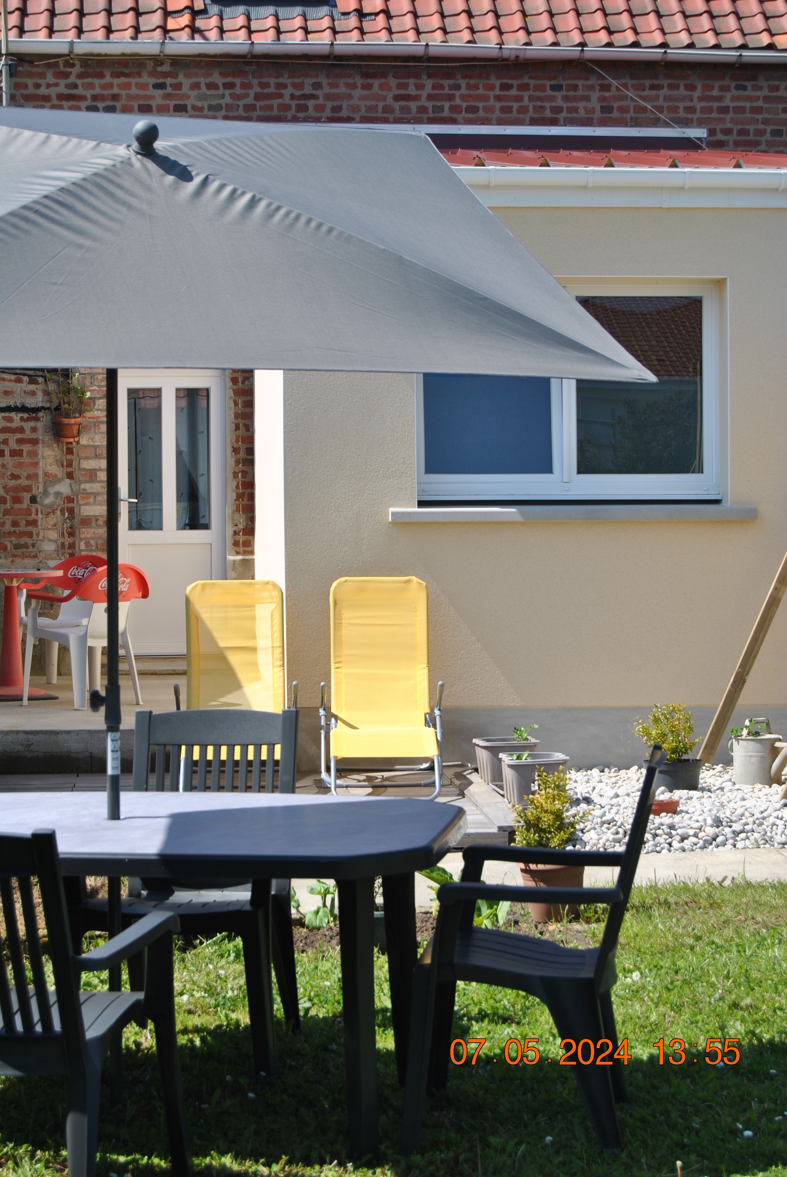 Au premier plan un espace repas en extérieur avec son mobilier, au deuxième plan un espace pour la petite sieste ou la digestion, et en arrière plan une cour avec son mobilier.