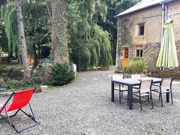 La façade arrière du gîte avec sa cour privative à la location, son salon de jardin, parasol, transats et vue sur l'étang.