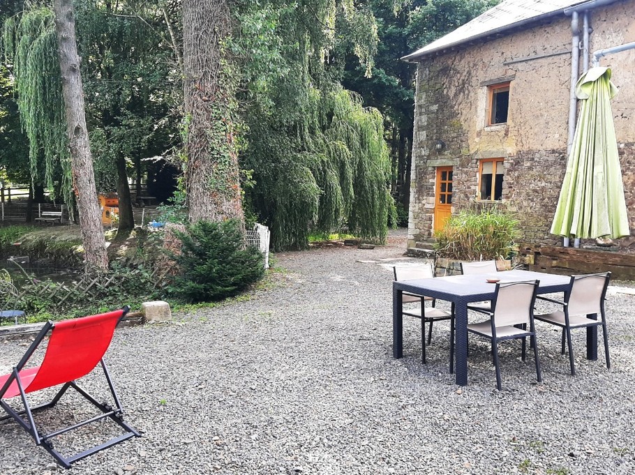 La façade arrière du gîte avec sa cour privative à la location, son salon de jardin, parasol, transats et vue sur l'étang.