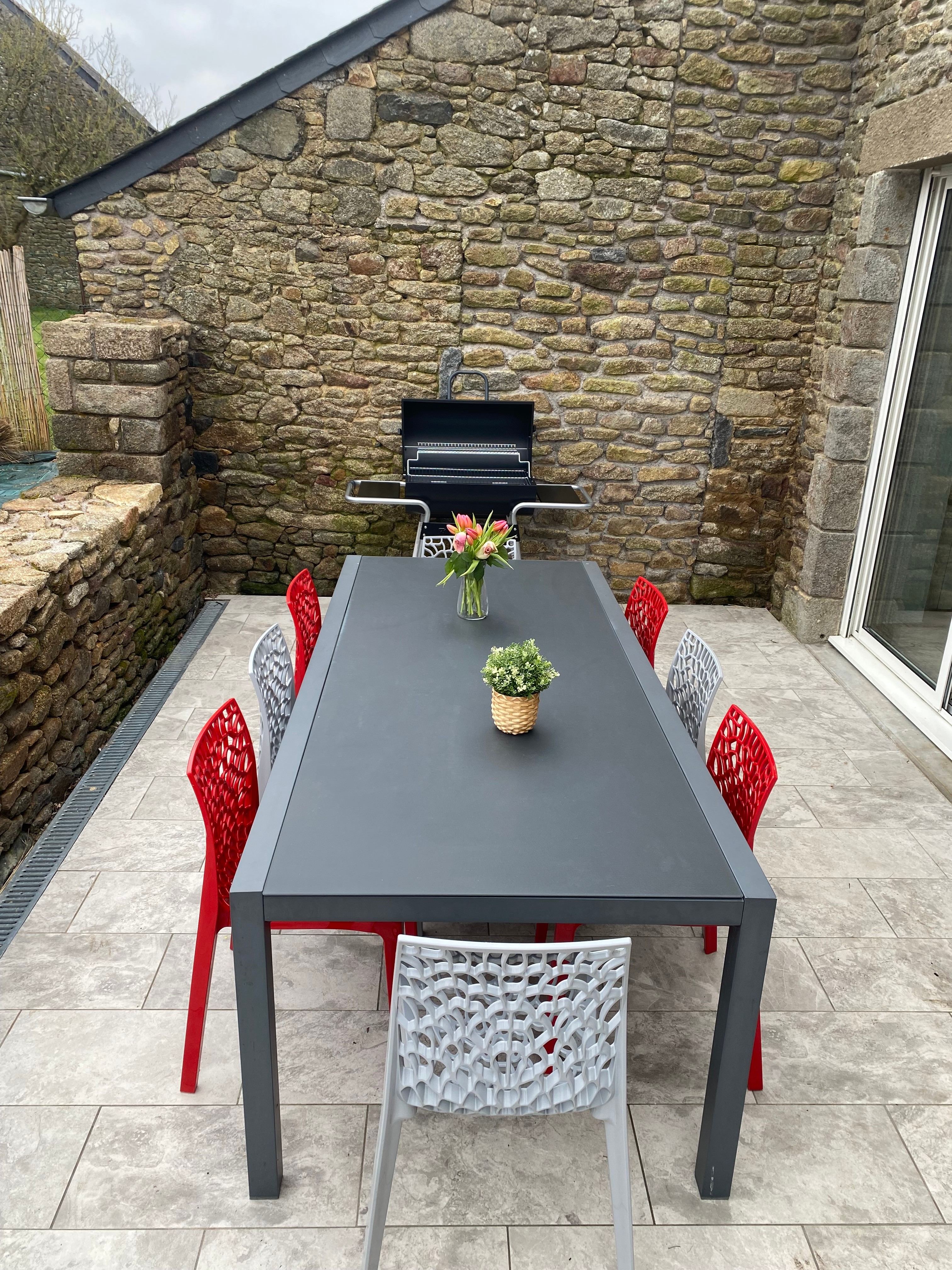 Terrasse avec table et salon de jardin. Dans le jardin, un boulodrome pour des parties de pétanque, un banc, une balançoire.