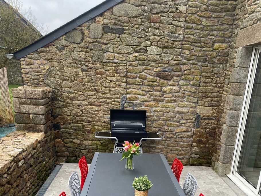 Terrasse avec table et salon de jardin. Dans le jardin, un boulodrome pour des parties de pétanque, un banc, une balançoire.