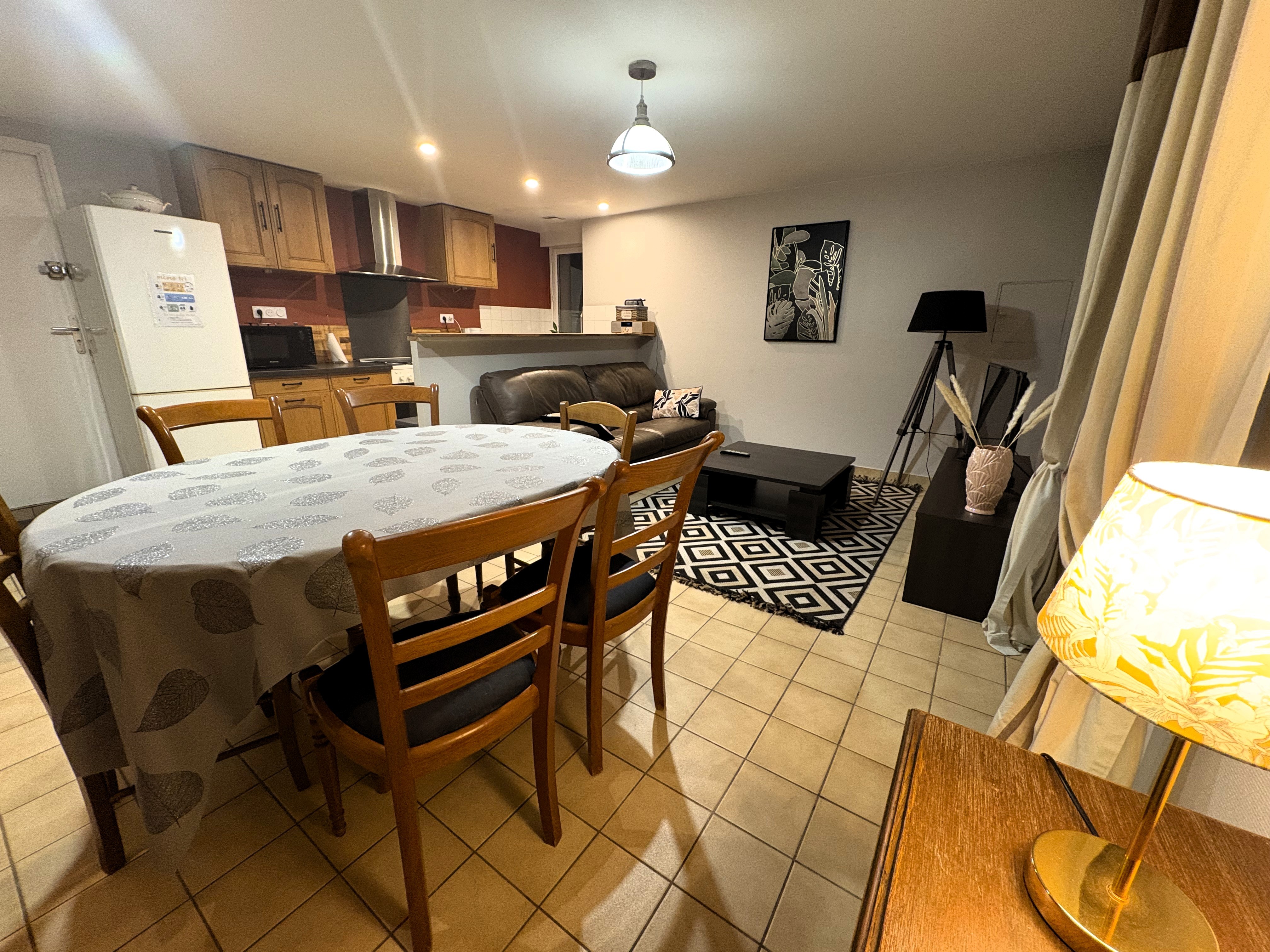 Pièce de vie au RDC avec coin cuisine, coin salon avec TV et coin séjour avec table à manger.