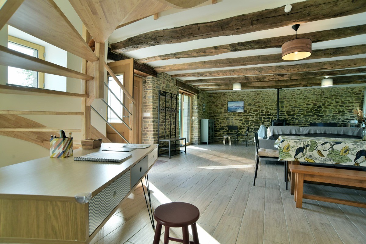 Grande pièce de vie avec poutres apparentes. En enfilade : coin salon, coin séjour, coin bureau et coin cuisine.