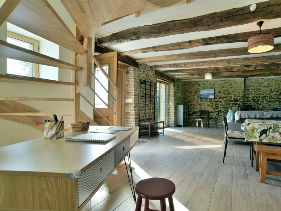 Grande pièce de vie avec poutres apparentes. En enfilade : coin salon, coin séjour, coin bureau et coin cuisine.