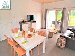 L'Entrée principal du chalet avec un salon avec télé, un coin repas et une cuisine équipée (– Plaques en vitrocéramique – Vaisselle – Réfrigérateur table top – Cafetière électrique – Micro-ondes – Table et chaises…). Terrasse abritée également visible.