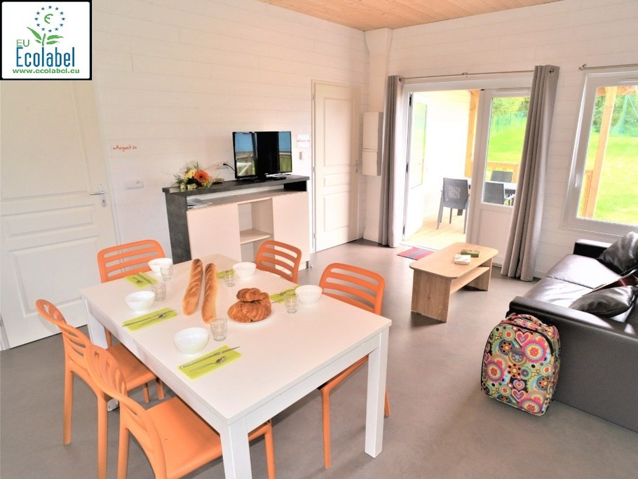 L'Entrée principal du chalet avec un salon avec télé, un coin repas et une cuisine équipée (– Plaques en vitrocéramique – Vaisselle – Réfrigérateur table top – Cafetière électrique – Micro-ondes – Table et chaises…). Terrasse abritée également visible.