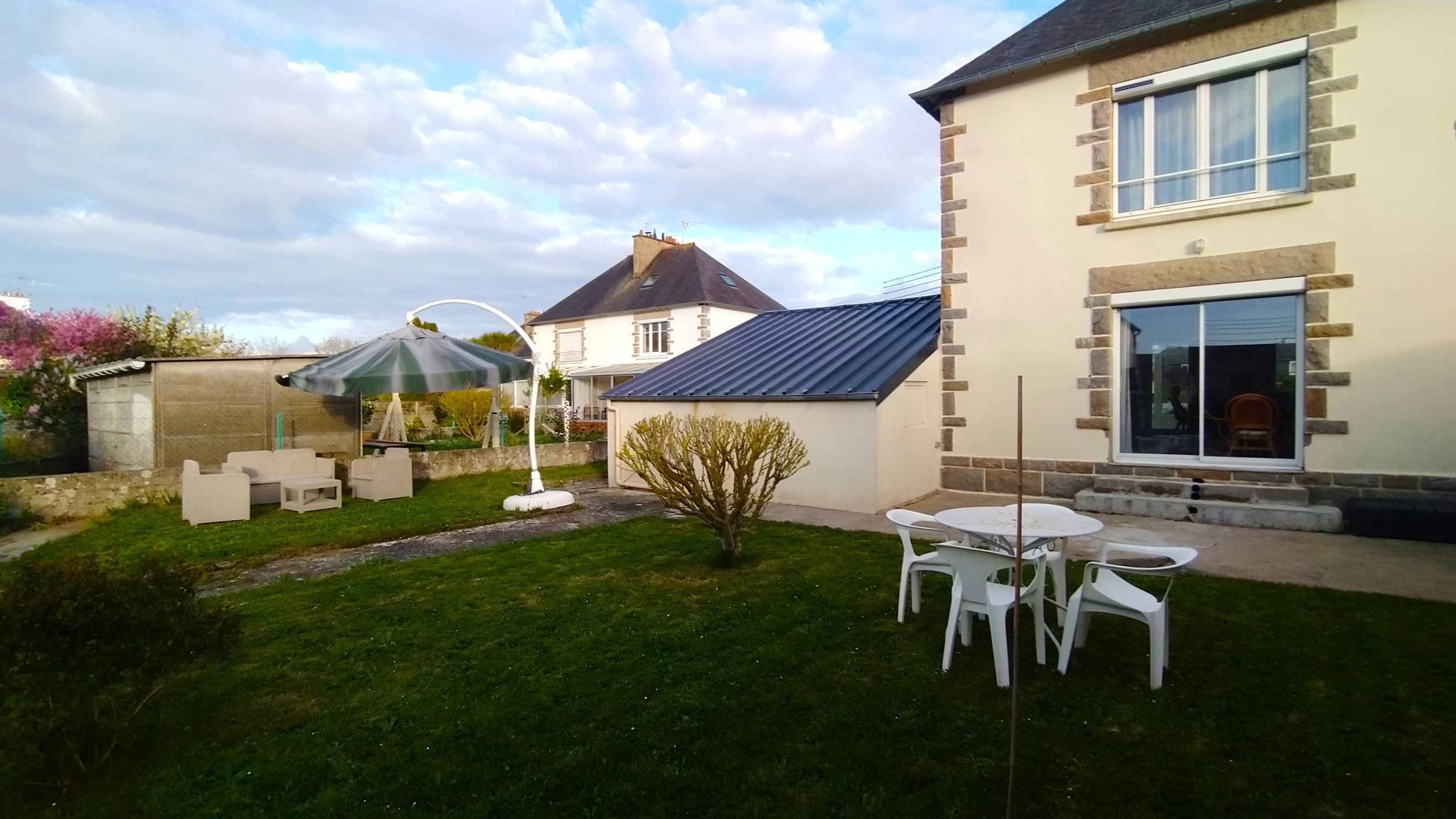 Jardin à l'arrière de la maison avec pelouse, terrasse, 2 salons de jardins haut et bas et parasol. Garage fermé pour stocker vos vélos, poussettes, paddle, etc.