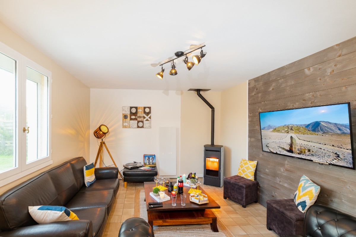 Salon avec canapé cuir, pouf, poêle à bois, TV 140cm connecté, éclairage d'ambiance, radiateur chaleur douce