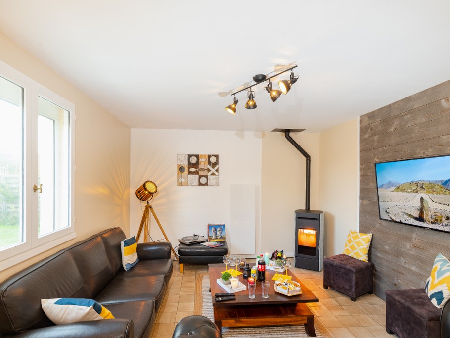 Salon avec canapé cuir, pouf, poêle à bois, TV 140cm connecté, éclairage d'ambiance, radiateur chaleur douce
