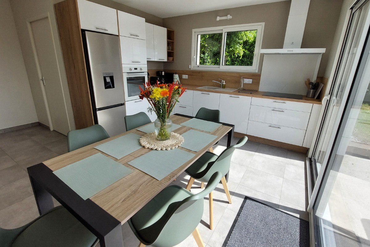 Cuisine moderne et entièrement équipée du gîte La Petite Maison, avec coin repas et baie vitrée donnant sur la terrasse.