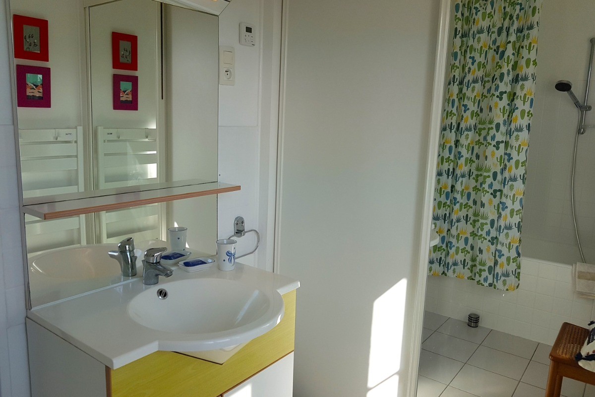 Salle de bain avec baignoire et meuble vasque. Vue mer.