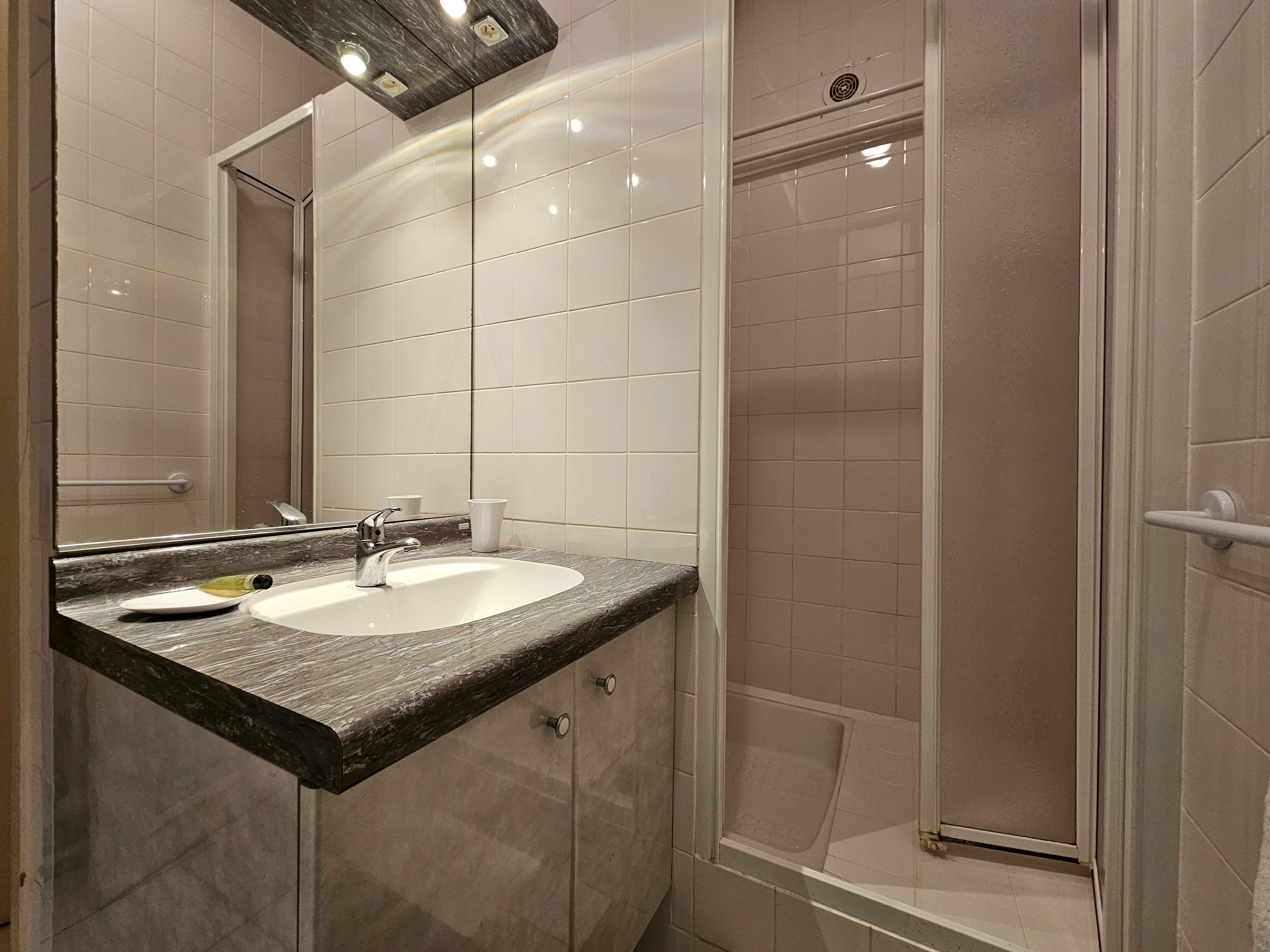 Salle d'eau avec douche grande dimension, meuble vasque et WC fermé.